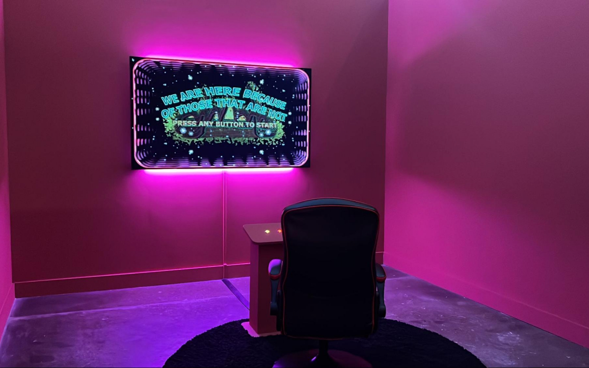 Image: Danielle Brathwaite-Shirley, WE ARE HERE BECAUSE OF THOSE THAT ARE NOT, 2020; Digital game displayed on projector; gaming chair; pink lights; and vinyl text. Courtesy of the artist.  Photo: Tina Rivers Ryan for Buffalo AKG Art Museum.